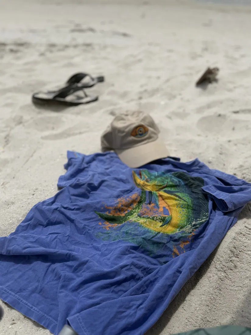 A tee and cap laid out on the sand